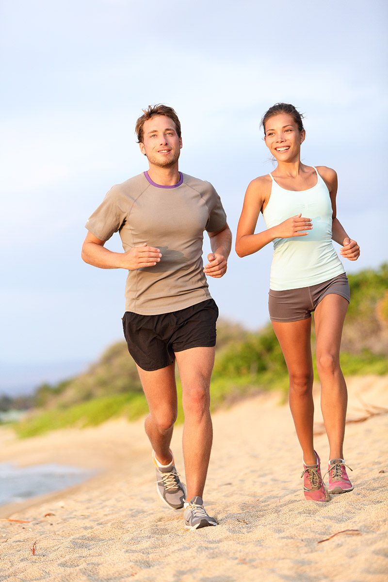 Running young mixed race couple jogging outside on beach happy smiling in summer sunset. Caucasian handsome male model and asian fitness female model.